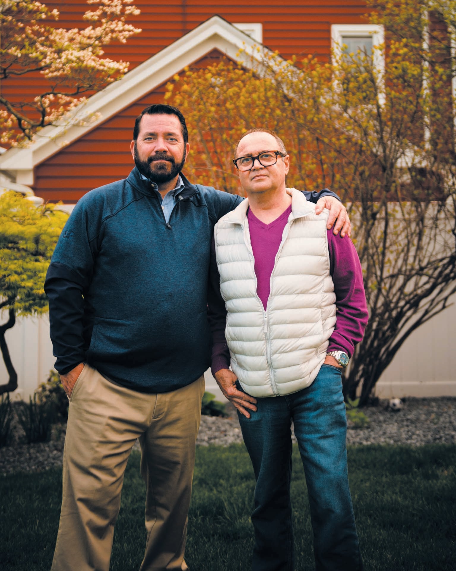 Portrait of two men standing outside with home in background.